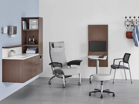 An exam room setting with Mora System casework on the wall in a dark brown finish, and an Intent Solution table located between a Nemschoff Nala Patient Chair and a Verus side chair.