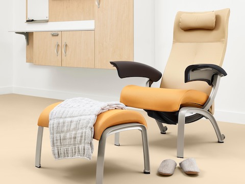 A patient room with a Nemschoff Nala Patient Chair and Ottoman upholstered in multiple fabrics with dark brown arms with Compass System casework on the wall.