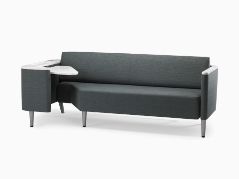 A Nemschoff Palisade Flop sofa in dark gray textile with white solid surface arms caps and white adjustable table with Durawrap top.