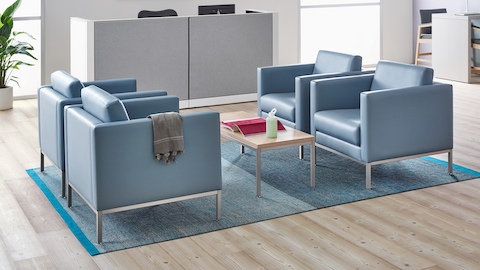 A waiting room featuring a Riva Coffee Table with a natural maple top and metallic silver base and Riva lounge chairs in blue textile with brushed metal legs.