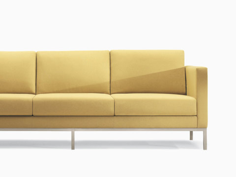 A Riva Sofa in a yellow textile with brushed metal legs.