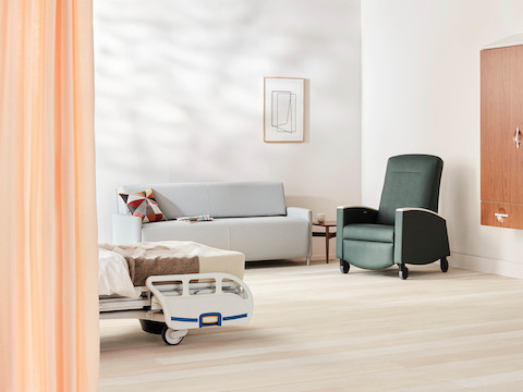 Patient room with Compass footwall in a medium walnut with a light gray Nemschoff Pamona Flop Sofa and a dark green Nemschoff Sahara Recliner.
