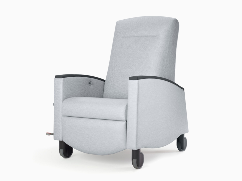 Nemschoff Sahara Recliner in a light gray upholstery with black arm caps and casters on white sweep, viewed at an angle. Nemschoff Sahara Recliner in a light gray upholstery with black arm caps and casters on white sweep, viewed at an angle.