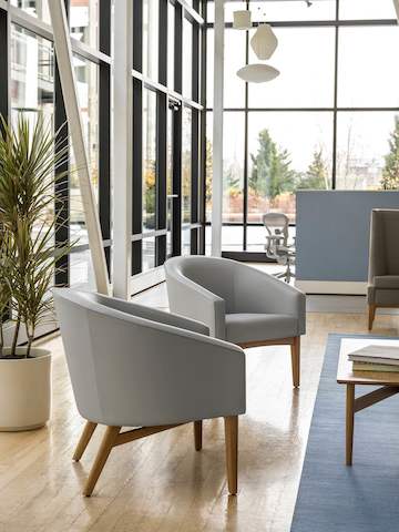 A waiting area with two Sophora Lounge Chairs in light blue textile with oak legs and base.