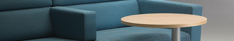 A close-up view of a Nemschoff Steps Lounge System in blue textile and a Steps round end table with a powder-coated base and laminate top.
