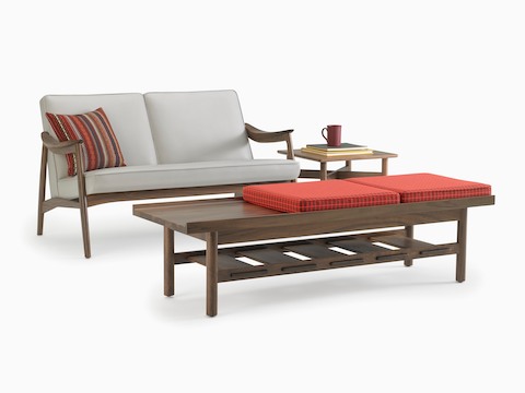An Aspen lounge settee in gray with a walnut base and arms with a Hemlock table in walnut and a Tamarack Table and Bench in walnut.