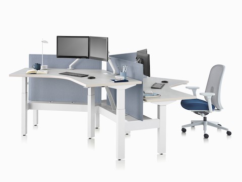 Sistema de mesas com regulagem de altura Nevi Link com superfícies de trabalho de 120 graus e cadeiras de escritório Lino cinzas e telas azul claro. Uma das três mesas está levantada até a altura para trabalhar em pé.