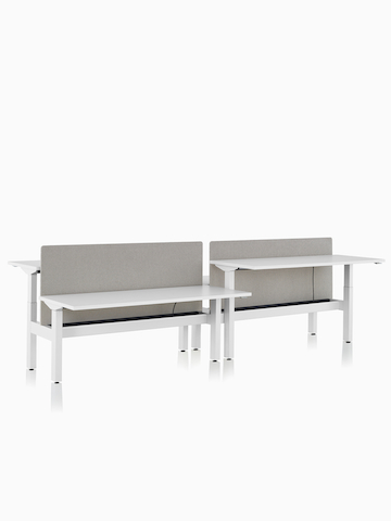 Sistema de mesas com regulagem de altura Nevi Link com superfícies de trabalho retangulares brancas e telas de privacidade cinzas. Duas das quatro mesas de trabalho estão levantadas até a altura de trabalhar em pé.
