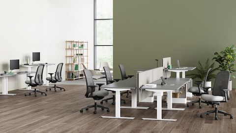 Un ambiente d’ufficio con scrivanie sit-stand Nevi configurate a varie altezze con sedute Lino grigie.