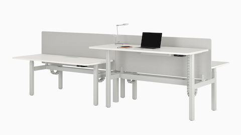 A four desk configuration of Nevi Sit-to-Stand Desks in white with gray fabric screens. Front right desk raised to standing height.