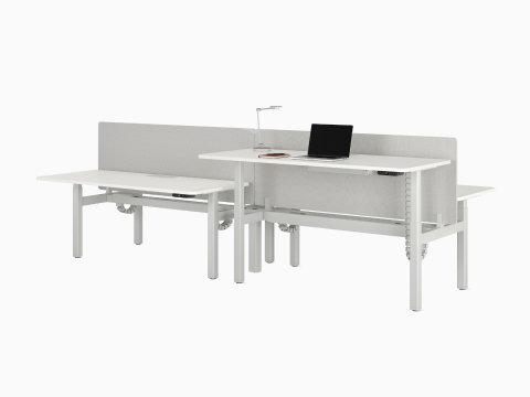 A four desk configuration of Nevi Sit-to-Stand Desks in white with gray fabric screens. Front right desk raised to standing height.