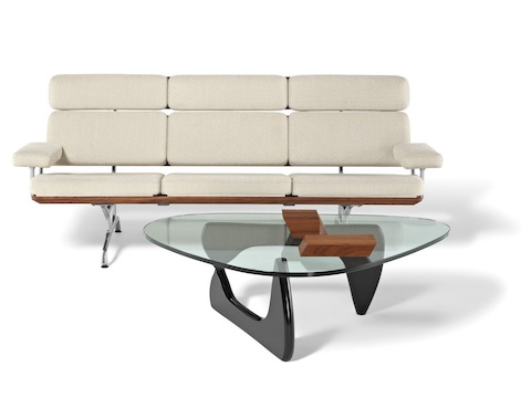 A Noguchi occasional table with a freeform glass top and black base complements an ivory-colored Eames Sofa. 