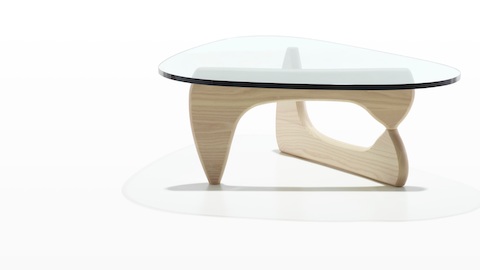 Una mesa auxiliar Noguchi con tapa de vidrio con forma libre y base curva en fresno blanco.