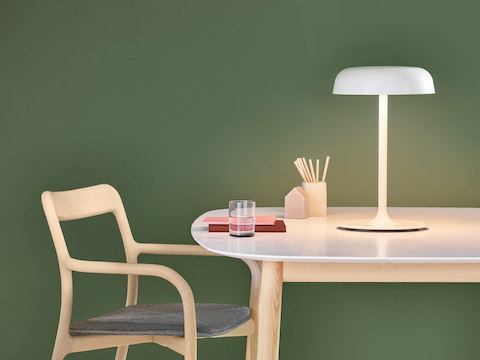 Luminária de mesa Ode branca ilumina uma mesa com tampo branco e cadeira para visitantes