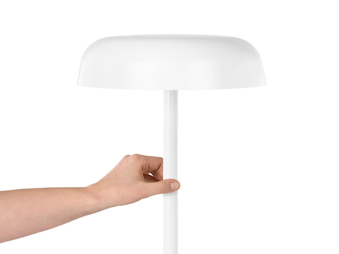 A hand touches the stem of a white Ode Lamp to turn it on or off.