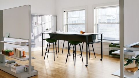 A black double sided OE1 Communal Table with casters, with OE1 Agile Walls in the foreground and OE1 Wall Rail and Board and OE1 Storage Trolley in the background.
