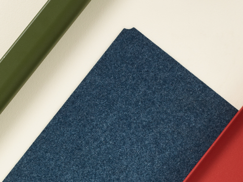 Una selección de los materiales de la Colección espacio de trabajo OE1, que incluye una superficie laminada en marrón claro, tarro de marcadores en gris, pata en verde, tela azul y estructura en rojo.