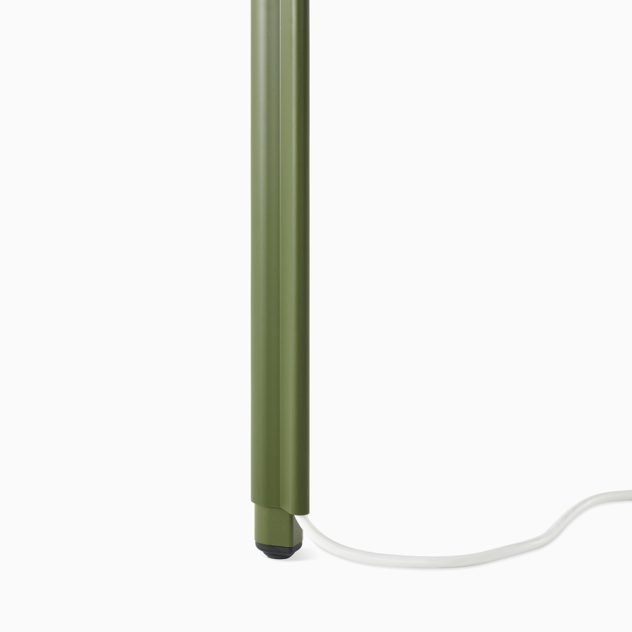 Imagen en primer plano de la pata en forma de lágrima de una mesa OE1 en verde y un organizador de cables en la plata saliente desde el fondo.