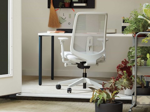 Uma mesa retangular OE1 com pernas azuis e superfície branca com uma cadeira Verus branca em uma configuração de home office.
