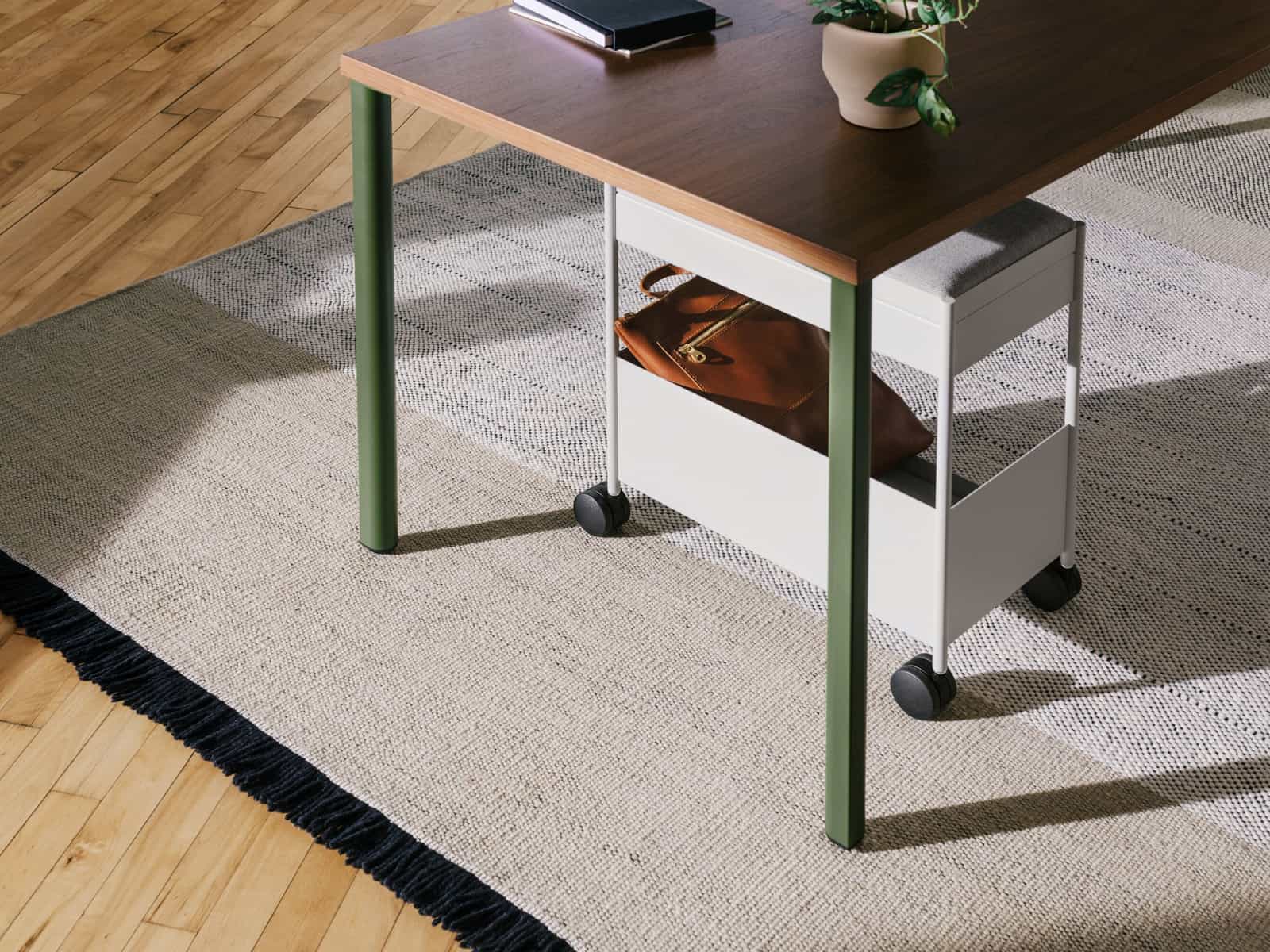 A grey, individual OE1 Storage Trolley with casters, nesting under an OE1 Rectangular Table with dark brown surface and green legs.