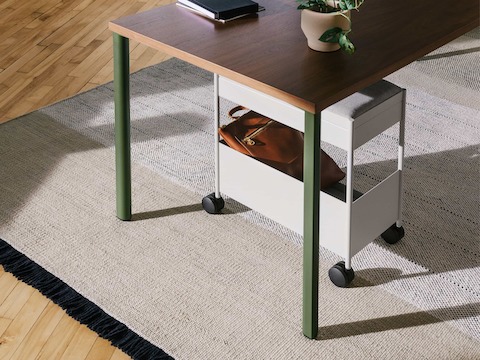 A grey, individual OE1 Storage Trolley with casters, nesting under an OE1 Rectangular Table with dark brown surface and green legs.