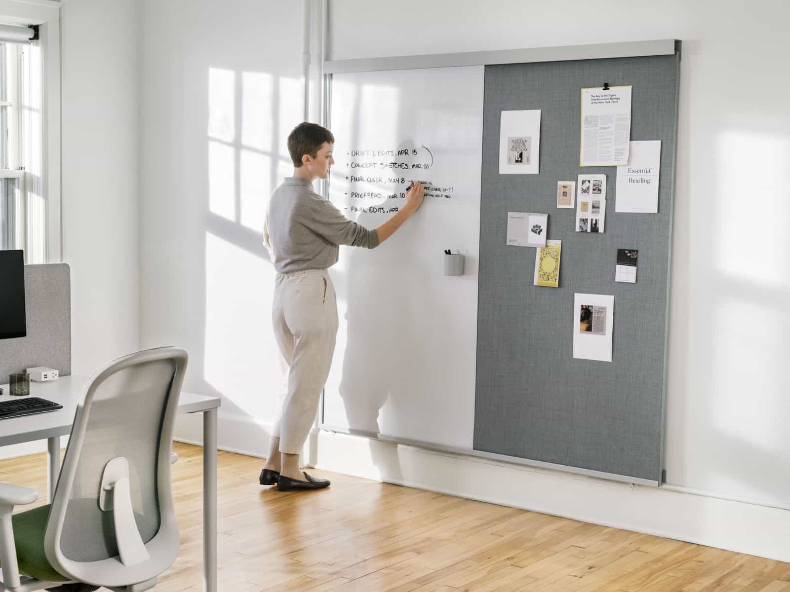 Una mujer escribiendo sobre un Riel y panel para pared OE1 con una mesa rectangular OE1 y una silla Lino en el frente.