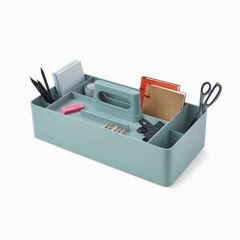 Coffret de rangement OE1 bleu clair avec crayons, bloc-notes et autres objets personnels, vus sous un angle.