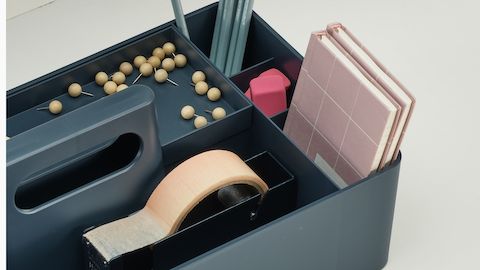 Detail of a dark blue OE1 Workbox with thumbtacks, notepads, and other small items, viewed from a top angle.