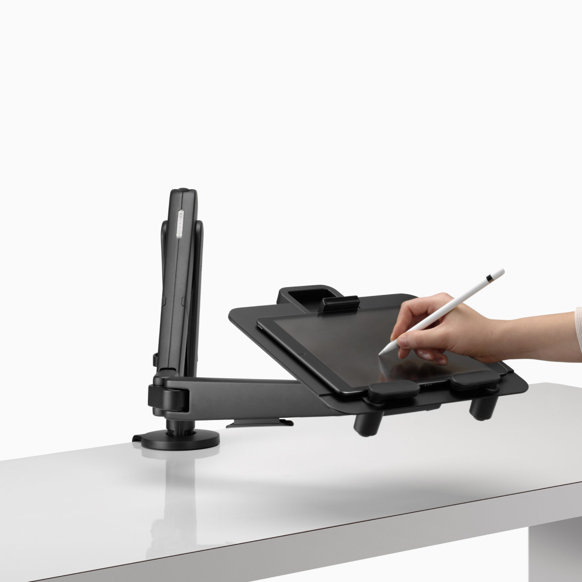 De hand van een persoon is afgebeeld terwijl deze tekent op een tablet ondersteund in landschapspositie door een Ollin-laptop en tabletsteun die is aangesloten op een zwarte Ollin-monitorarm.