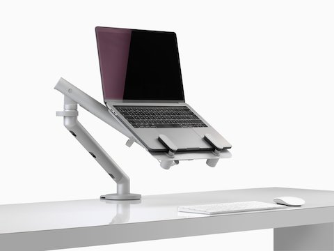 Um laptop aberto e elevado na linha dos olhos, apoiado por um suporte para laptop Ollin e um braço para monitor Flo.