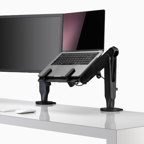 Tela de monitor e um laptop aberto e elevado na linha dos olhos, apoiado por um suporte para laptop e um braço para monitor Ollin.