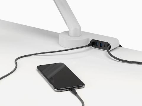 A desk with a mobile phone charging cable and a data cable connected to an Ondo Connectivity Module. A desk with a mobile phone charging cable and a data cable connected to an Ondo Connectivity Module.