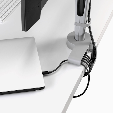 Hoekaanzicht toont een hoek van een monitorscherm met stroomkabels die van de aangesloten monitorarm worden geleid en door een Ondo-connectiviteitsmodule naar een laptop en onder een bureau.