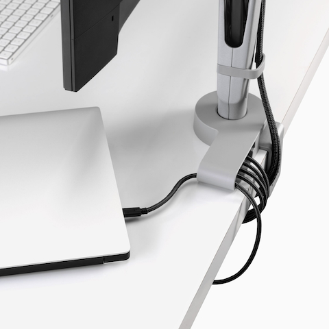Angled view showing a corner of a monitor screen with power cables routed from a connected monitor arm and through an Ondo Connectivity Module to a laptop and under a desk. Angled view showing a corner of a monitor screen with power cables routed from a connected monitor arm and through an Ondo Connectivity Module to a laptop and under a desk.