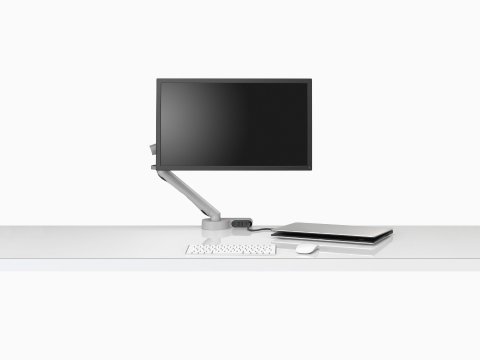Vooraanzicht van een scherm bevestigd aan een Flo-monitorarm ingebouwd met een Ondo-connectiviteitsmodule op een bureau aangesloten op een halfgesloten laptop.