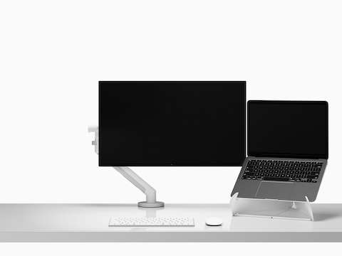 工作台面上，显示器挂臂和显示器旁边的Oripura笔记本电脑支架上放着一台打开并抬高的笔记本电脑
