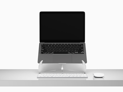 Um laptop aberto elevado na linha dos olhos, em um suporte para laptop Oripura, colocado sobre uma mesa com ferramentas de trabalho.
