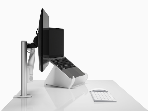 Side view of a monitor arm and screen next to open Laptop raised on an Oripura Laptop Stand on top of a worksurface with work tools. Side view of a monitor arm and screen next to open Laptop raised on an Oripura Laptop Stand on top of a worksurface with work tools.