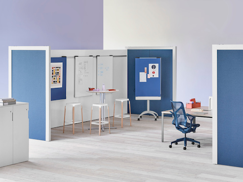 Two Overlay room dividers placed across each other with tables and chairs in between with markerboards in the interior and dark blue fabric on the exterior.