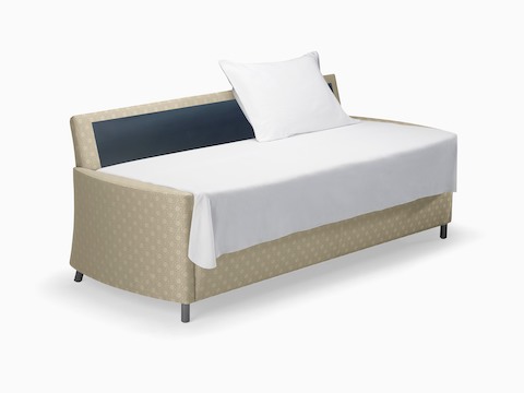 A beige-patterned Pamona Flop Sofa converted into a sleep surface with a sheet and pillow.