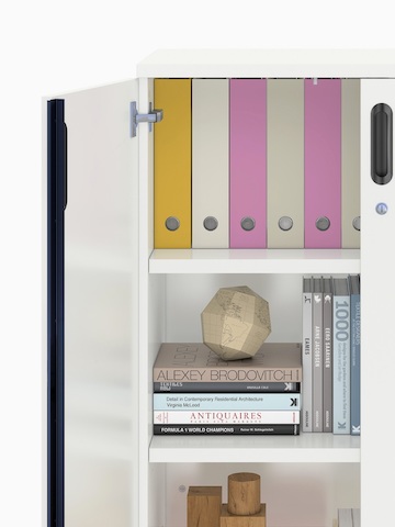 Vista parziale di un'unità di immagazzinamento Paragraph, concentrandosi su una porta a battente aperta e libri e raccoglitori all'interno. Vista parziale di un'unità di immagazzinamento Paragraph, concentrandosi su una porta a battente aperta e libri e raccoglitori all'interno.