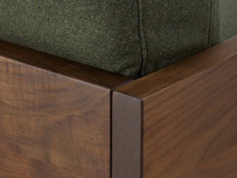 A detail view of the Pawson Drift Sofa Groups back corned with solid wood walnut and a green textile.