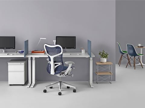 Un espacio de trabajo con dos mesas rectangulares Renew Sit-to-Stand, cuatro pantallas laterales personales en azul, pedestal metálico Tu, una silla Mirra 2 en azul y mesas auxiliares.