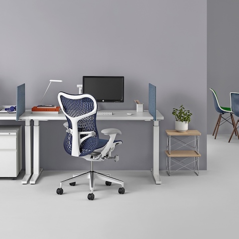 A workspace with two rectangular Renew Sit-to-Stand Tables, blue Personal Side Screens, Tu Metal pedestal, a blue Mirra 2 Chair, and end tables.