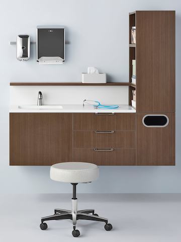 A Physician Stool in light textile is featured in front of a dark finish wall-hung Mora System.