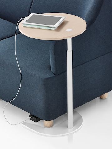 A close up version of a blue upholstered seat accompanied by a height adjustable Plex Work Table with a laminate wood top and white base with a tablet plugged into the optional power unit attached to the seat. A close up version of a blue upholstered seat accompanied by a height adjustable Plex Work Table with a laminate wood top and white base with a tablet plugged into the optional power unit attached to the seat.