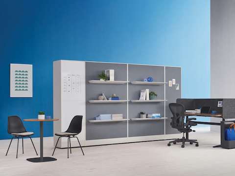 An Atlas height adjustable desk with an Aeron Chair next to Port Storage System with shelves and white board features. A casual meeting space is featured in the foreground.