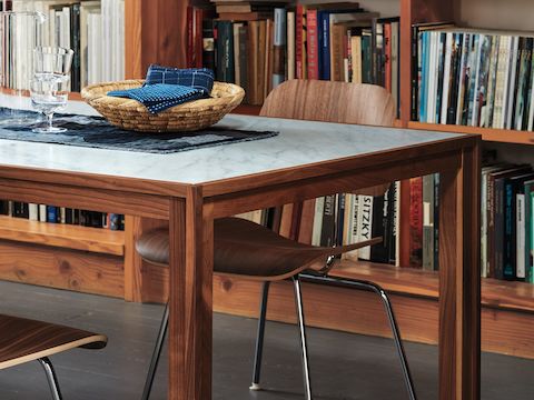 An Eames Molded Plywood Dining Chair with a metal base sits at a rectangular table with bookshelves in the background.
