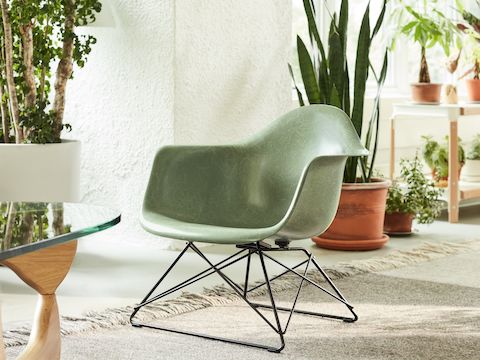 A close-up view of the Eames Molded Fiberglass Armchair with a low wire base in a casual living setting next to a Noguchi Table.