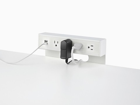 A variety of cords and adapters plugged into the USB port and standard power sockets of a white, table-mounted Logic power adapter.